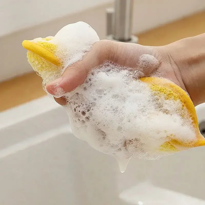 Hand holding yellow 2 pieces double sided kitchen cleaning sponges covered in soap foam over a sink
