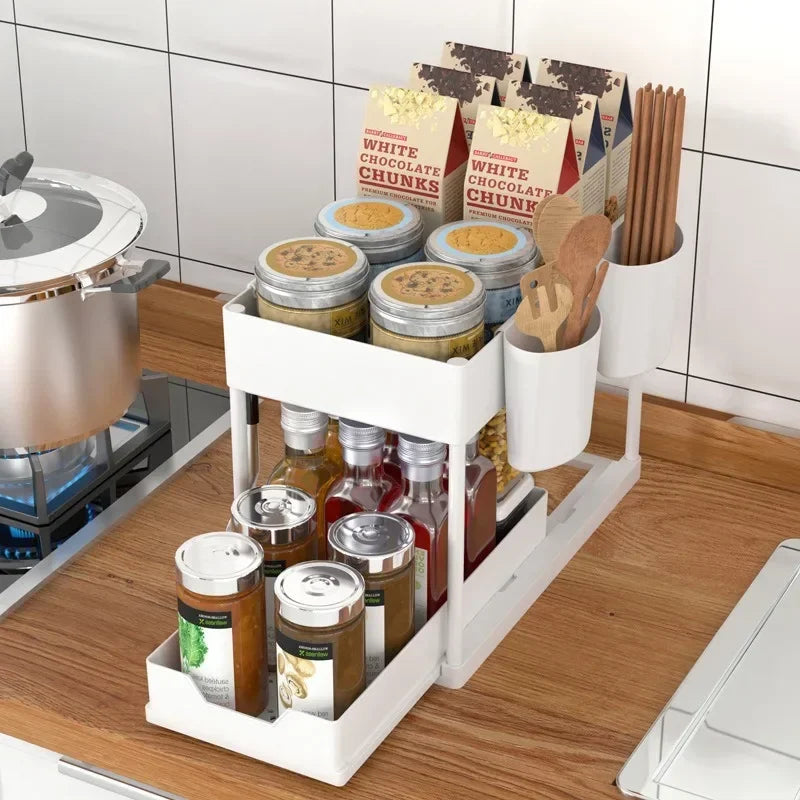 Clarify.pk white 2 tier kitchen organizer holding jars, spice cans, and wooden utensils on countertop