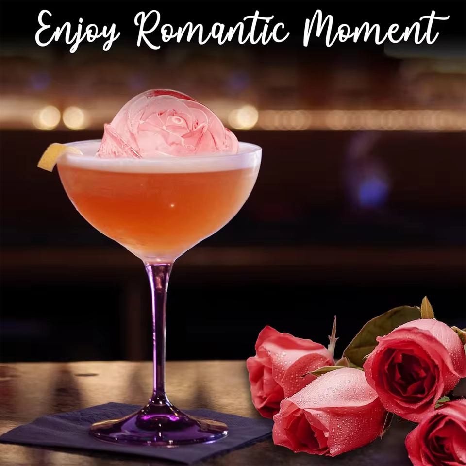 Pink cocktail with a 3D rose ice cube mold in a tall glass next to fresh pink roses on a dark table