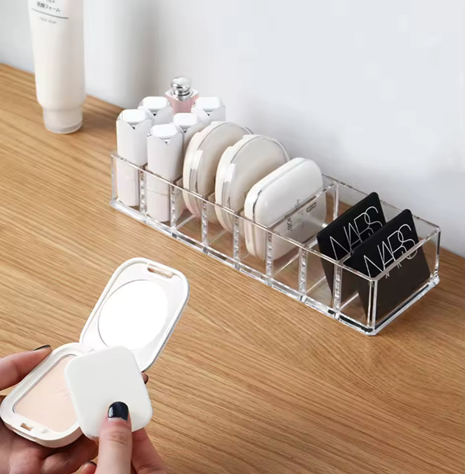 Clear 8 compartment organizer by Clarify.pk holding makeup compacts and lipsticks on wooden surface