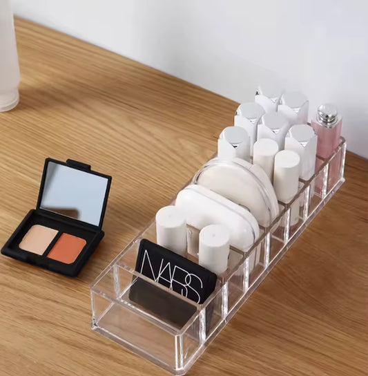 Clear 8 compartment organizer holding makeup items like lipsticks and compact powders on wooden surface