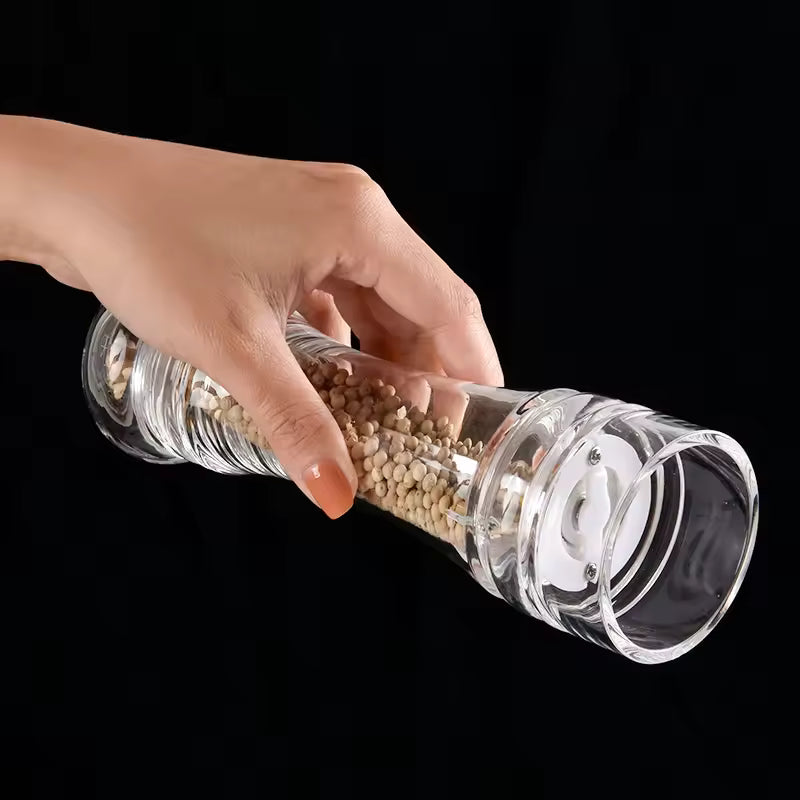Hand holding a transparent acrylic manual paper grinder filled with white peppercorns against black background