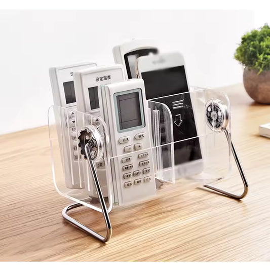 Clear acrylic remote control holder by Clarify.pk organizing multiple remotes and a smartphone on a wooden surface