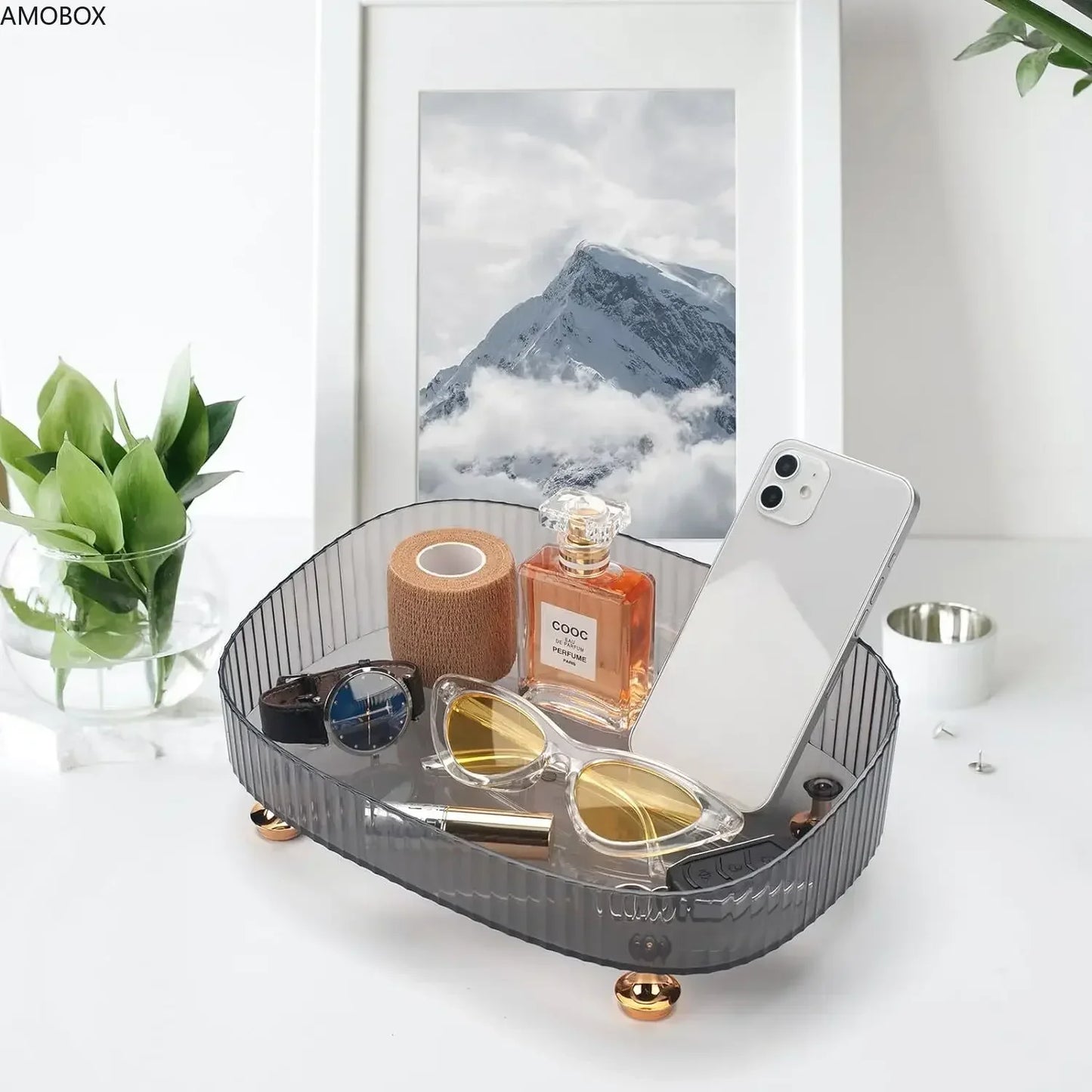 Gray transparent dresser storage box holding sunglasses, perfume, phone, and accessories on white table