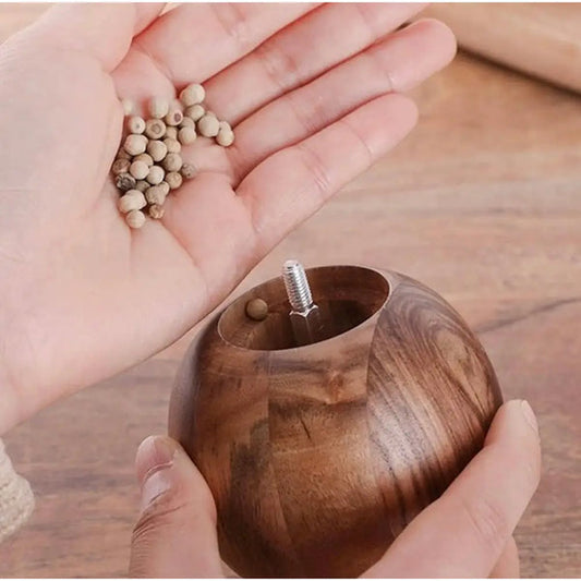 Hands pouring white peppercorns into round walnut wooden pepper grinder with removable top and smooth finish