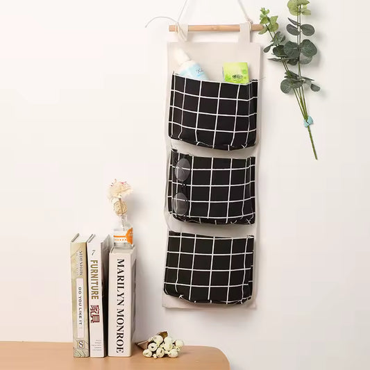 Clarify.pk black and white hanging wall storage organizer with three pockets holding items on a white wall