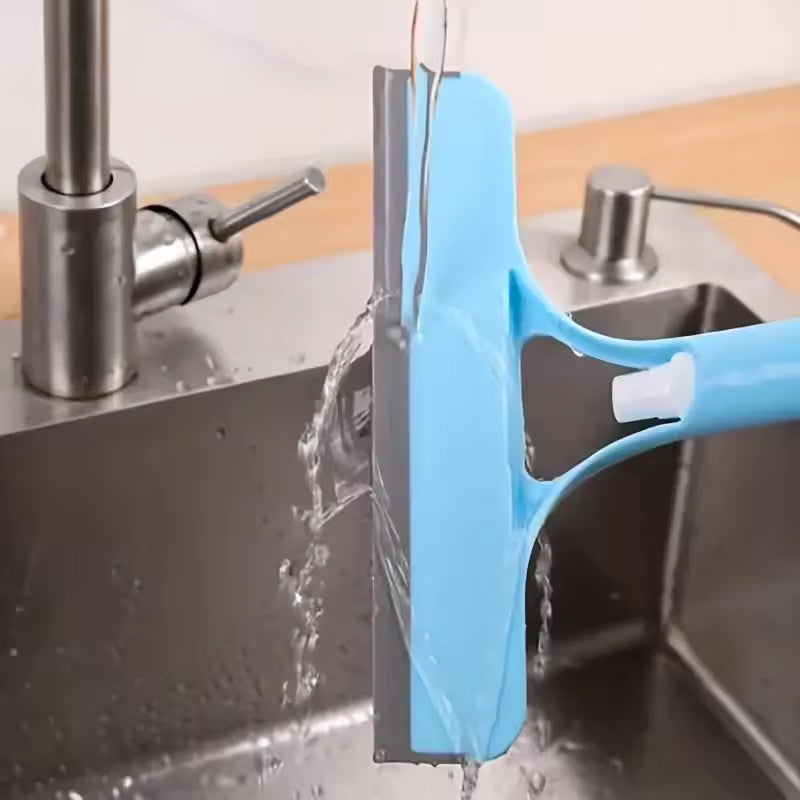 Blue 3-in-1 shower scraper being rinsed under running water near a stainless steel sink