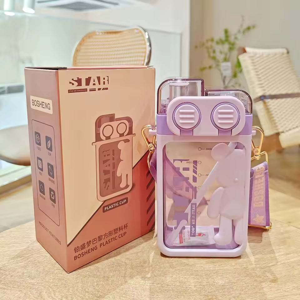 Purple cartoon bear water bottle with clear sections and matching strap beside pink product box