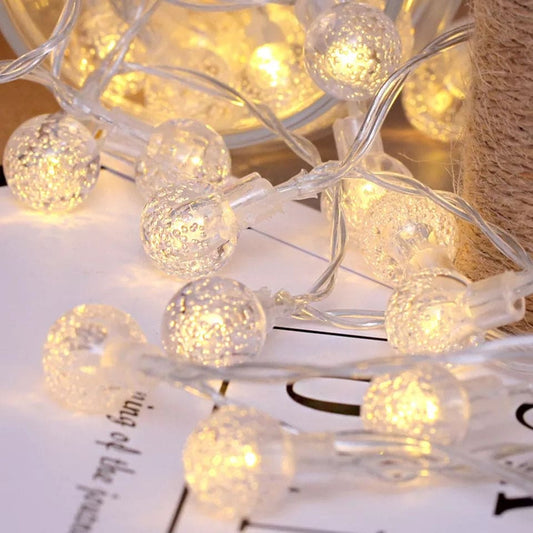 Clarify.pk bubble ball LED string lights glowing warmly on a white surface with clear wiring