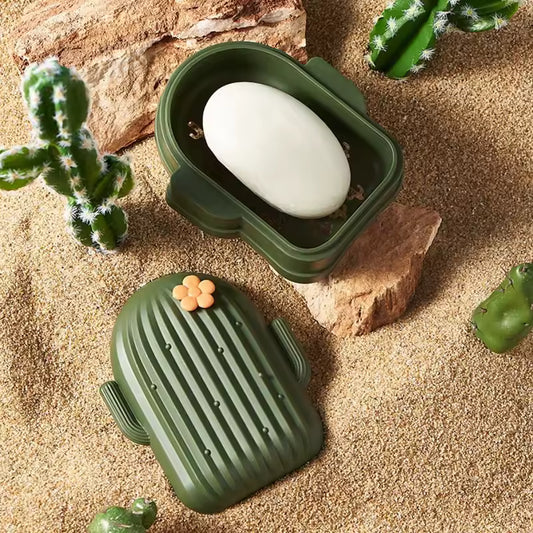 Green cactus shape soap dish holder with lid and white soap on sandy surface with decorative cacti