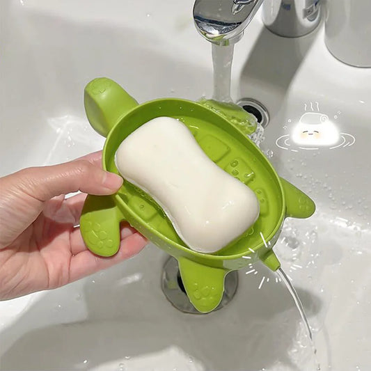 Green cartoon turtle soap holder with drainage, holding a white soap bar over a sink