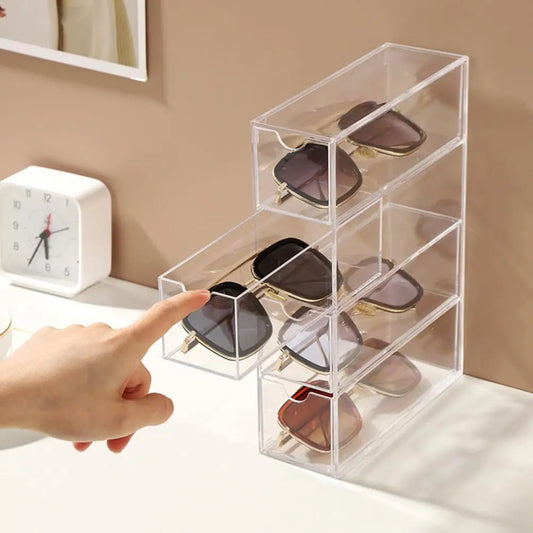 Clear acrylic sunglasses storage box with three drawers holding multiple pairs of sunglasses