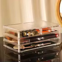 Clear makeup organizer with drawers holding lipsticks and jewelry on a vanity table
