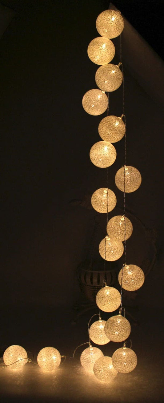 Warm white cotton ball string lights hanging vertically with soft glowing orbs against a dark background