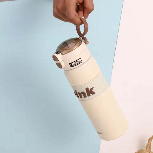 Cream-colored stainless steel sports water bottle with flip cap and carrying loop held by hand
