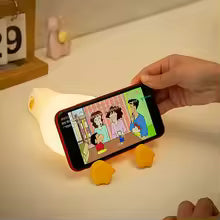 Cute duck night light holding a phone displaying a cartoon scene on a desk
