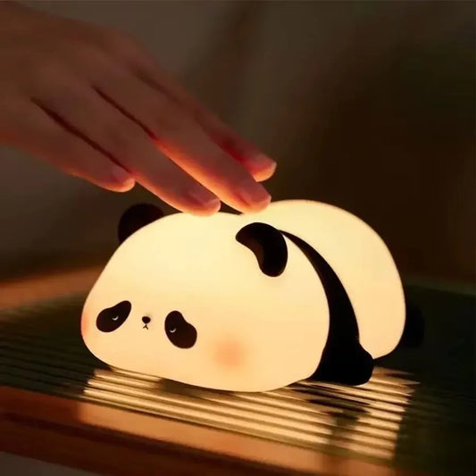 Hand touching a glowing cute panda desk lamp with soft warm light on a wooden surface