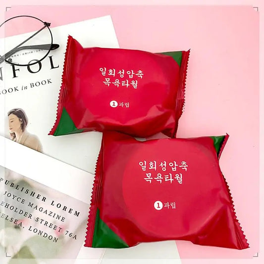 Clarify.pk disposable bath towel in red and green packaging placed on a pink surface next to a book and glasses