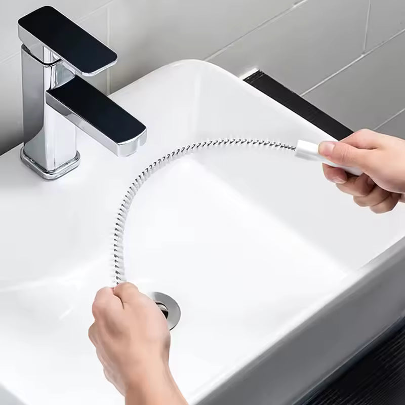 Person using a drain clog remover tool to clear sink drain under modern faucet in white bathroom