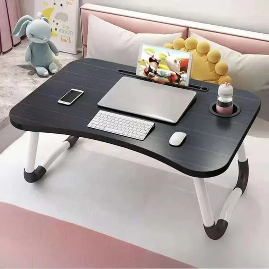 Clarify.pk foldable Laptop desk in black with white legs on a bed holding a laptop keyboard mouse and phone