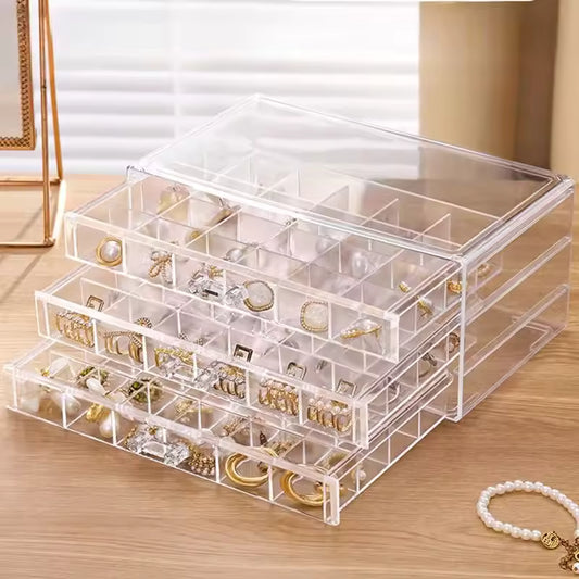 Clear acrylic drawer jewelry storage case with multiple compartments holding earrings and rings