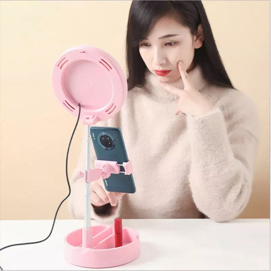 Foldable selfie stick with ring light in pink held on table with phone and lipstick holder
