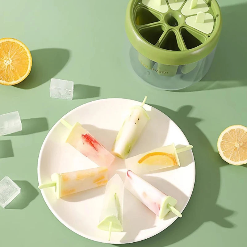 Green ice cream maker with six homemade popsicles on white plate and sliced citrus fruits