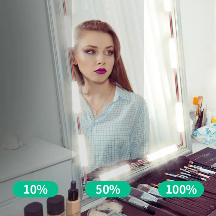 Woman using LED vanity mirror lights for perfect makeup application with brushes and cosmetics nearby