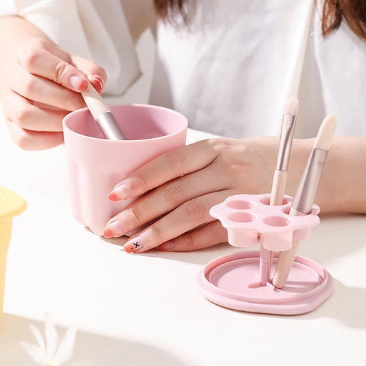 Pink makeup brush cleaner box with slots holding brushes and a hand cleaning a brush inside the box