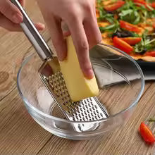 Mini stainless steel grater by Clarify.pk grating cheese into a glass bowl on wooden table
