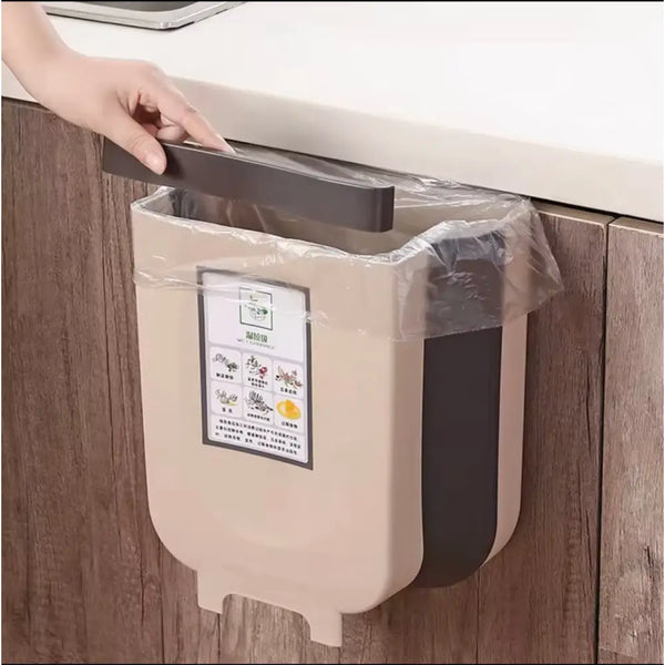 Beige and black wall mounted kitchen trash bin attached to wooden cabinet with hand lifting lid
