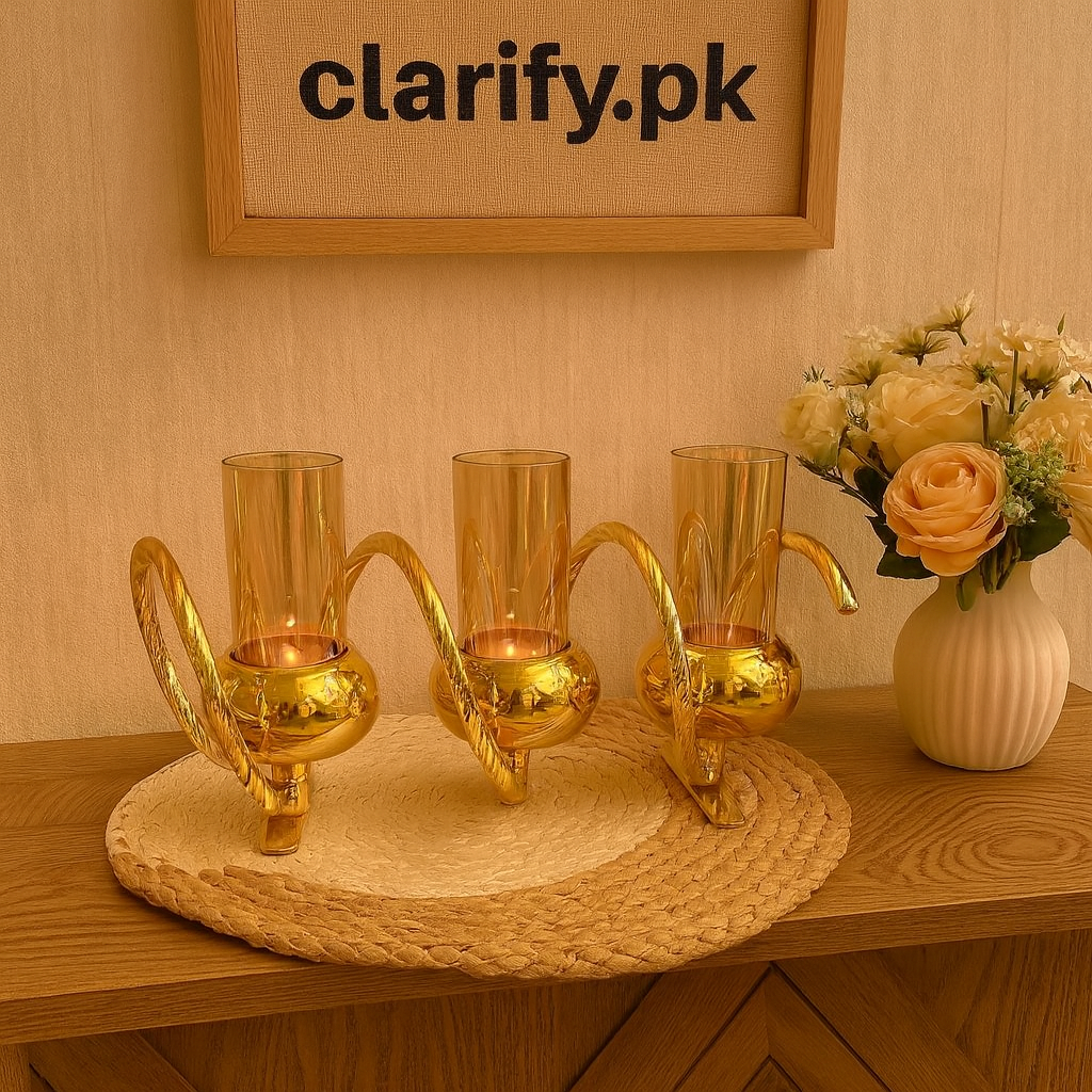 Elegant golden triple glass candle holder with curved handles displayed on a woven mat near decorative flowers