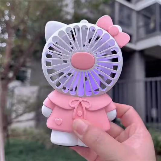 Hello Kitty handheld fan in pink outfit held outdoors with visible fan blades and bow