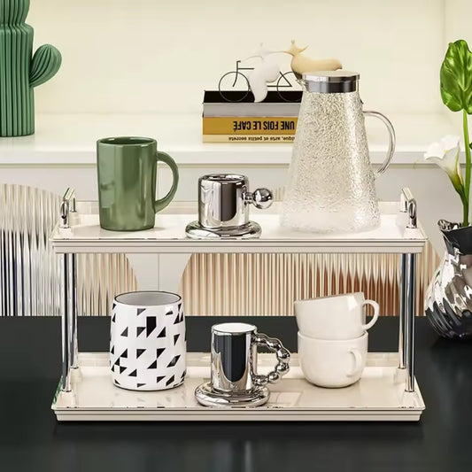 2 tier desktop cup rack organizer in silver holding multiple mugs and a glass pitcher on a black countertop