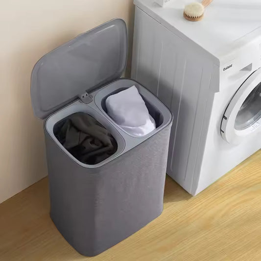Gray Japanese style clothes hamper with dual compartments next to a washing machine on wooden floor