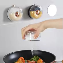 Hand placing a clear kitchen magnetic spice jar on a magnetic wall rack above a cooking pan