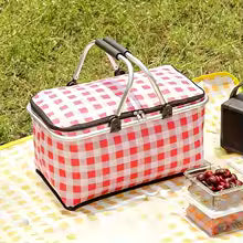 Large foldable picnic basket with red and white checkered pattern placed on yellow picnic blanket outdoors