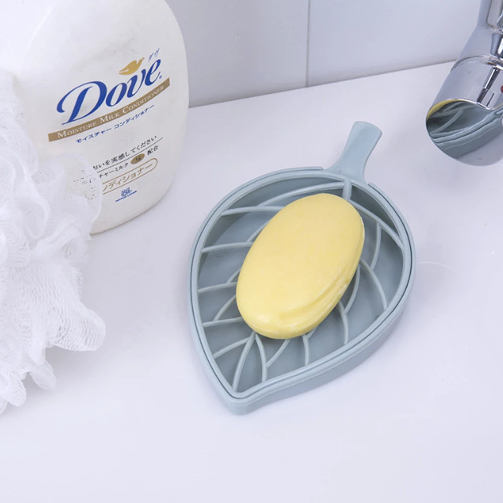 Light blue leaf shape soap dish holding a yellow soap bar next to bathroom faucet and Dove moisturizer