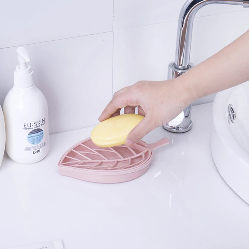 Hand placing yellow soap on pink leaf shape soap dish next to sink with faucet and lotion bottle