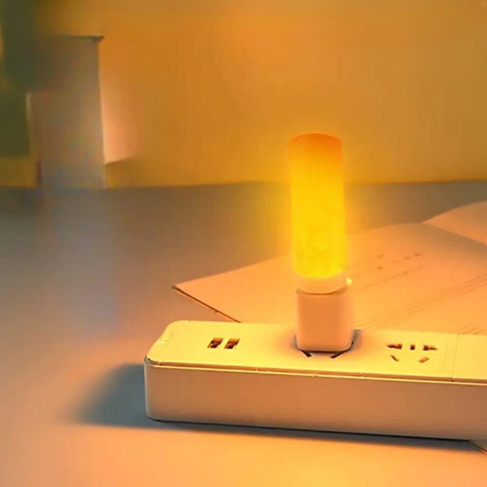 Clarify.pk LED flame effect night light plugged into a white power strip casting warm yellow light