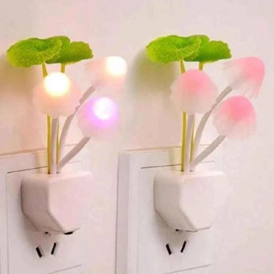 Home de LED mushroom night light with glowing pink and white mushroom caps and green leaves plugged into wall outlet