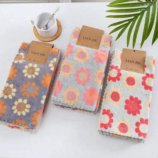 Three folded floral cotton face towels with colorful daisy prints in gray pink and cream for bathroom use