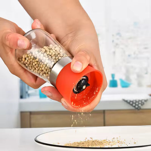 Clarify.pk manual salt and pepper grinder with transparent body and red base being used to grind pepper onto a plate