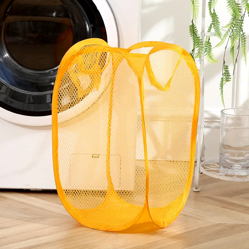 Yellow mesh foldable laundry basket by Clarify.pk placed next to a washing machine on a wooden floor