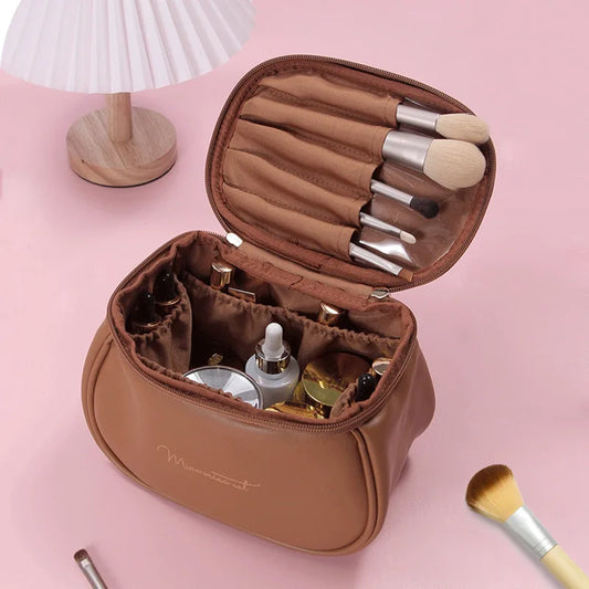 Brown portable makeup case with zipper holding brushes and cosmetic bottles on pink surface