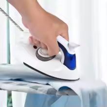 Mini handheld steam iron in white and blue being used on light blue fabric on ironing board