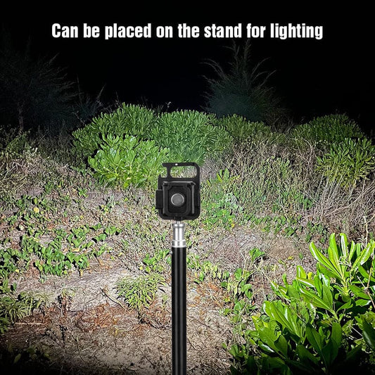 Mini LED flashlight keychain mounted on a stand illuminating outdoor bushes at night
