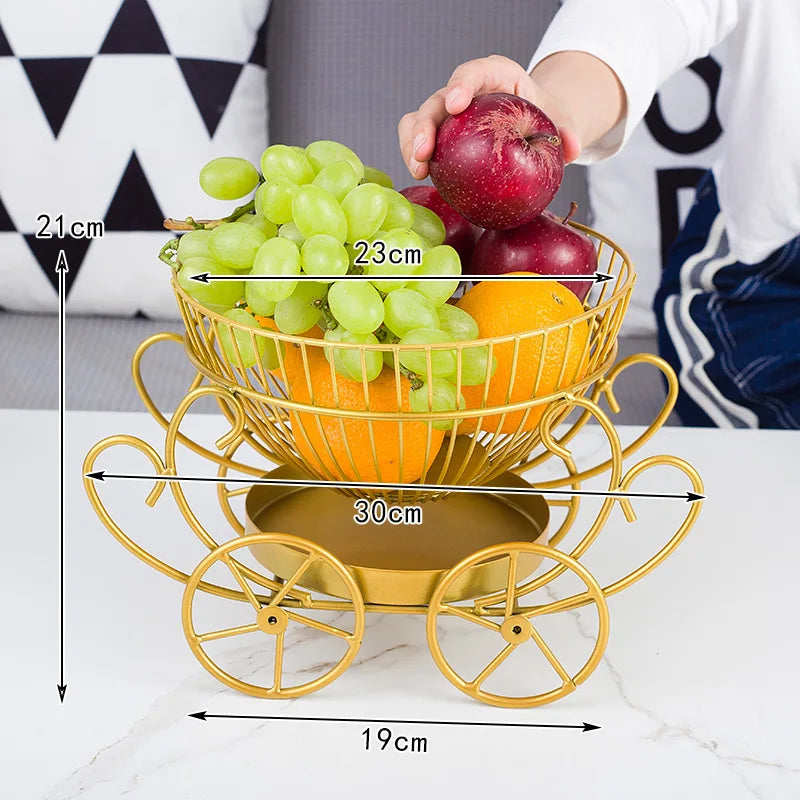 Clarify.pk modern fruit basket in gold metal with wheels holding grapes, apples, and oranges on table