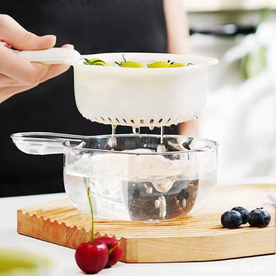 White multi-functional drain basket draining water from grapes into a transparent bowl on a wooden cutting board