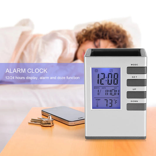 Silver multifunctional alarm clock with pen holder showing time and temperature on bedside table